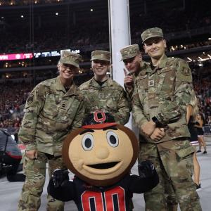 Brutus Buckeye poses with an ROTC cadets at a Buckeyes night football game