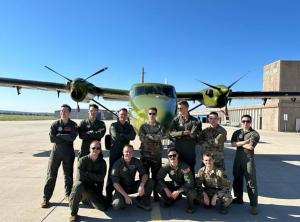 A pilot team poses outside in front of an carrier plane with propellors.